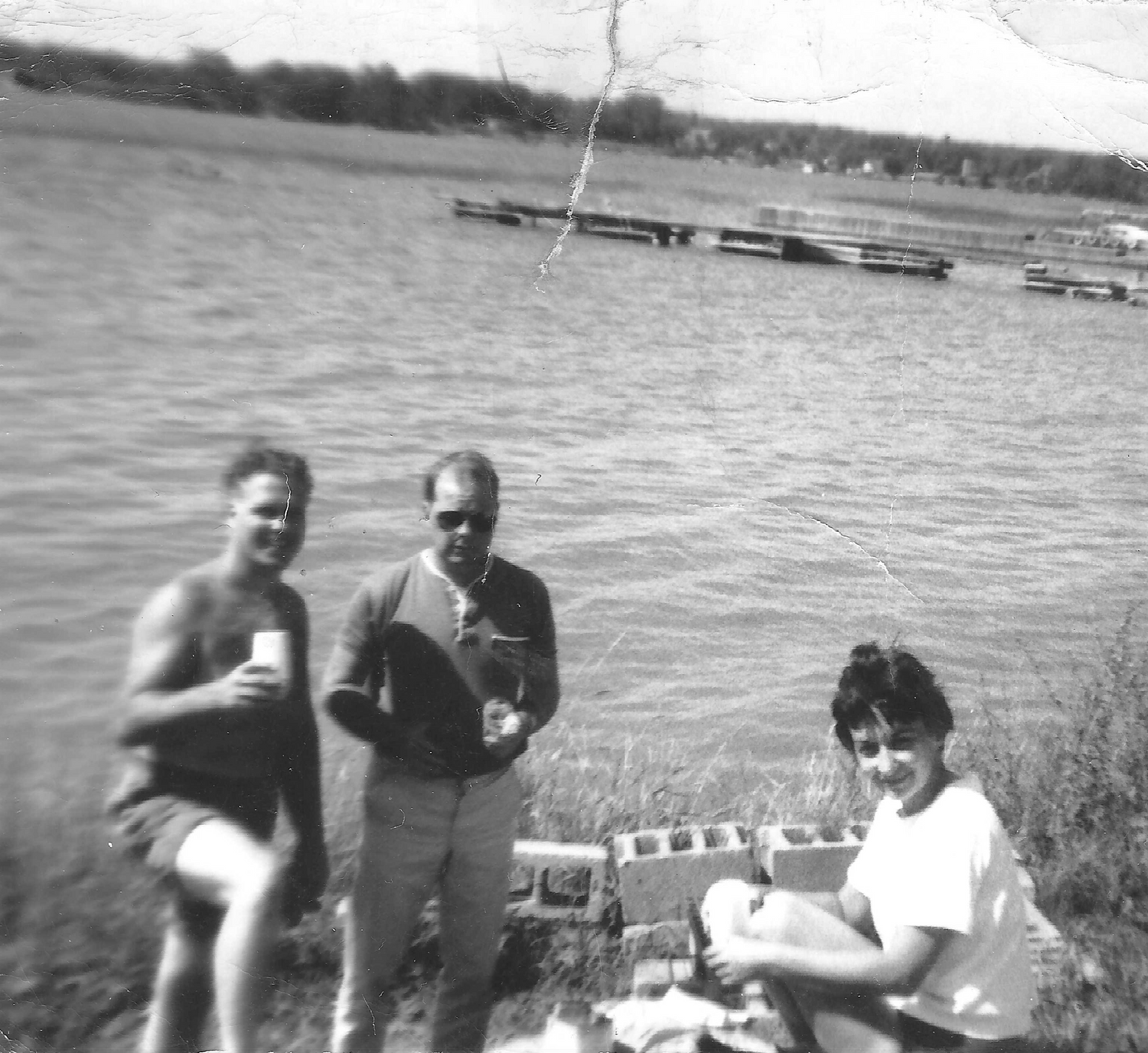 Three people by a lake with boats in the background